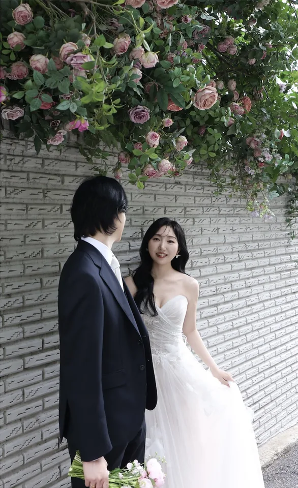 꽃이 핀 벽 앞에 나란히 서 있는 신랑과 신부