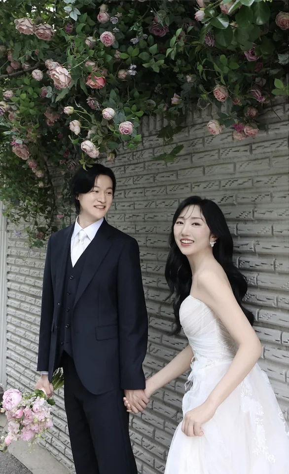 꽃이 핀 벽 앞에서 함께 웃는 신랑과 신부