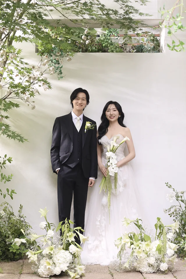 흰 꽃 장식 사이에 나란히 서 있는 신랑과 신부
