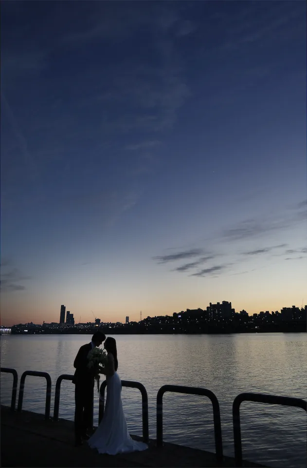 푸른 밤 강가에 나란히 서 있는 신랑과 신부